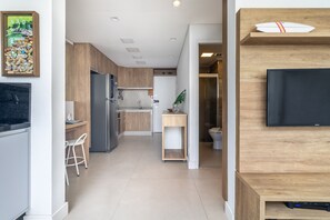 Eine moderne Küche mit Einbauofen, einem Essbereich mit einem weißen Stuhl und einem an einer Holzwand montierten Fernseher.