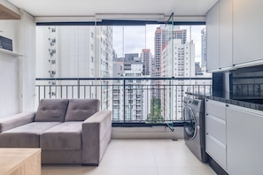 Ein Balkon mit einer Couch, einer Waschmaschine und Blick auf hohe Gebäude.