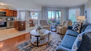 Eine moderne Küche mit Holzausstattung, ein Essbereich mit Stühlen, ein runder Couchtisch und ein Wohnzimmer mit Sofa und Lampe.