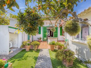 Une cour avec un chemin, des plantes en pot et un bâtiment aux volets verts.