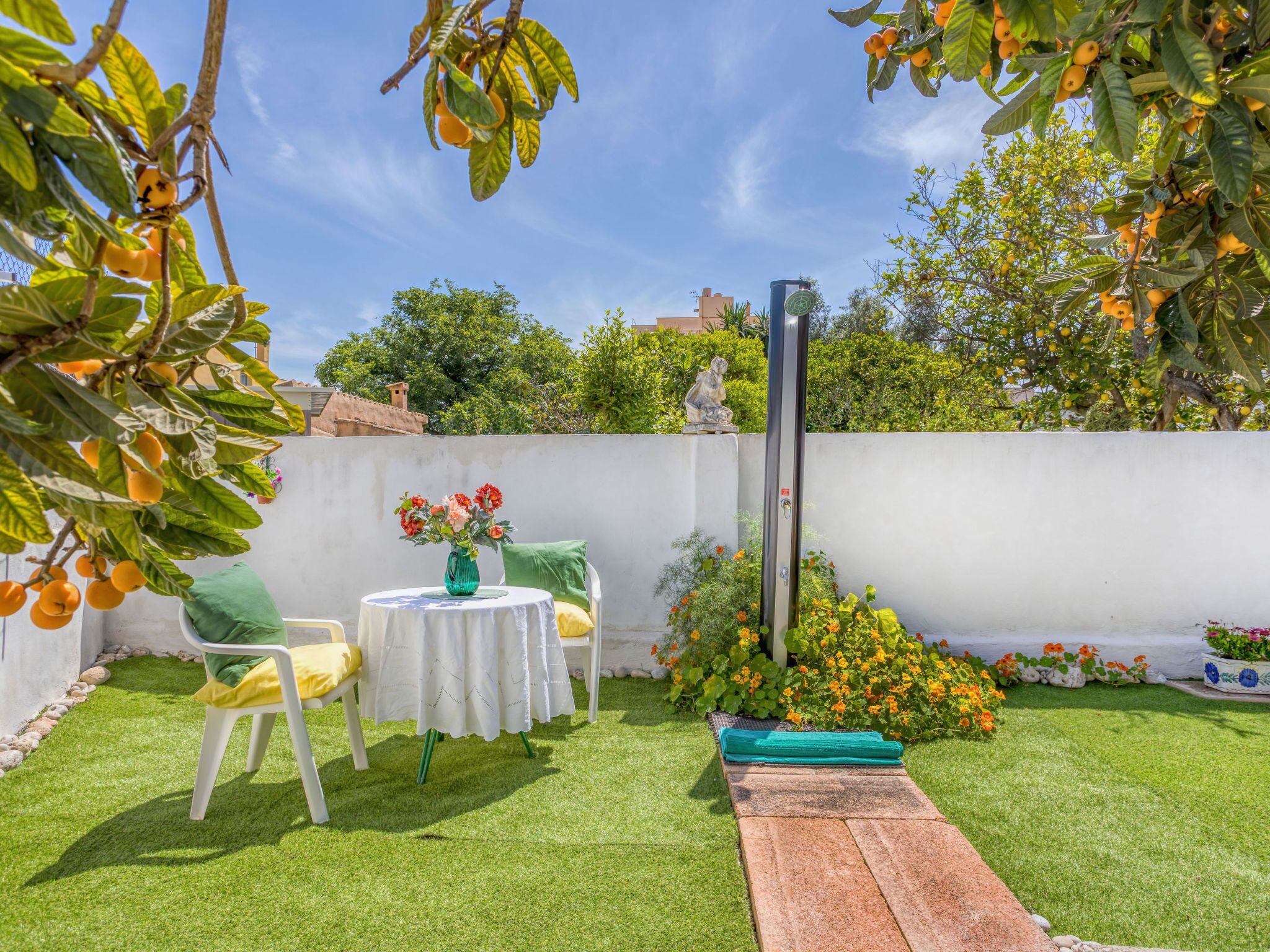 A patio with a table and chairs, a statue, and a garden with flowers and fruit trees.