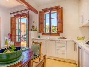 A kitchen with wooden cabinets, a dining table with chairs, and a window with a view of greenery. - Casa Vileta by Interhome (Vileta)