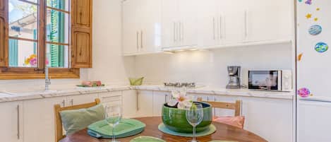 Una cocina moderna con armarios blancos, una mesa de comedor de madera con individuales verdes y un refrigerador con imanes decorativos.