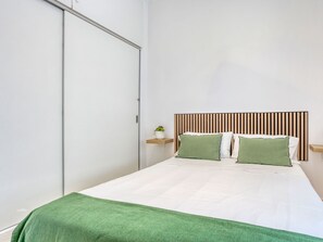 A bedroom with a bed, a wooden headboard, a bedside table with a plant, and a green throw blanket. - Casa Vileta by Interhome (Vileta)