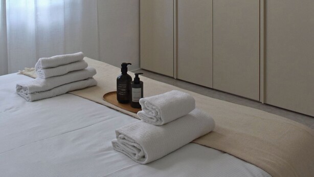 Ein Hotelzimmer mit einem Bett, ordentlich gefalteten Handtüchern, einer Lotionflasche und einem Holztablett.