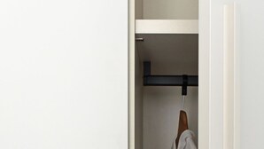 Ein weißer Kleiderschrank mit Kleiderstange und einer teilweise geöffneten Tür.