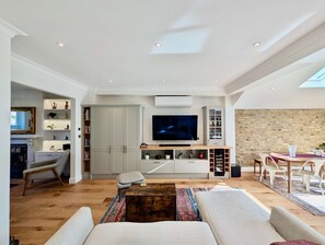 A modern living room with a flat-screen TV, wooden flooring, and a brick wall. - Cosy Bright 2-bed House in Earlsfield (London)