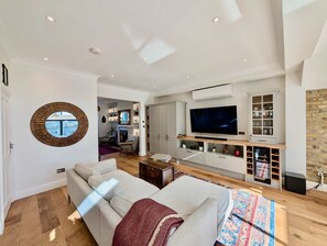 A modern living room with a sofa, TV, and built-in entertainment unit. - Cosy Bright 2-bed House in Earlsfield (London)