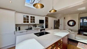 A modern kitchen with white cabinetry, a central island, and a hanging pendant light. - Cosy Bright 2-bed House in Earlsfield (London)