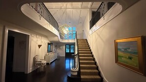 En imponerende hall med trappe, lysekrone og et maleri på væggen.