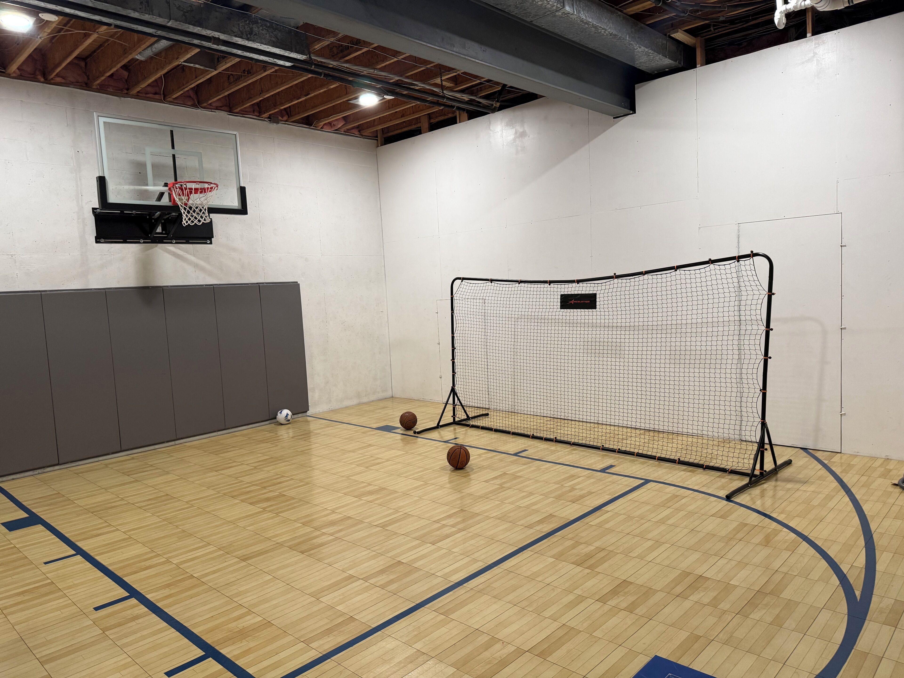 A basketball court with a netted goal area, a basketball hoop, and a ball on the floor.