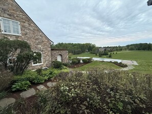 Una casa de piedra con jardín, zona pavimentada y vistas a un parque y edificios lejanos.