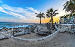 A beachside area with a hammock, lounge chairs, and palm trees. - Oceanfront Luxury Villa w/ Private Pool & Hot Tub (Cabo San Lucas)