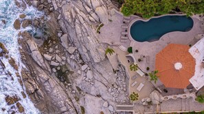 An aerial view of a coastal property with a swimming pool, a circular outdoor seating area, and a staircase leading to a covered terrace. - Oceanfront Luxury Villa w/ Private Pool & Hot Tub (Cabo San Lucas)