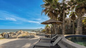 Ein Poolbereich mit Liegestühlen und einem Sonnenschirm, mit Blick auf eine felsige Küstenlinie und das Meer.