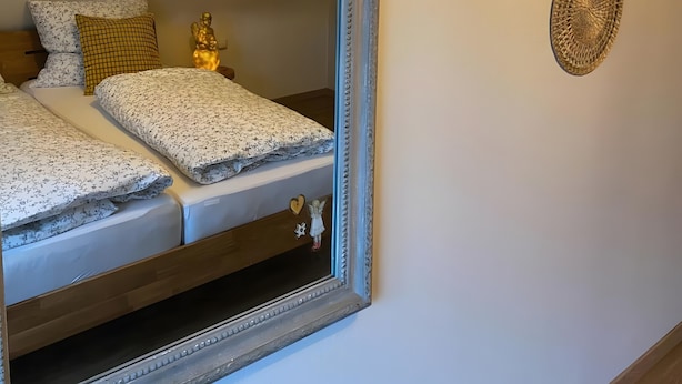 Ein Bett mit einem Spiegel darüber, eine goldene Statue und drei gewebte Wanddekorationen.