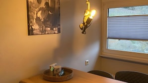 Ein Essbereich mit einem Holztisch, schwarzen Stühlen, einer hängenden Leuchte, einem gerahmten Bild und einem Fenster mit Jalousien.