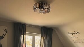 Ein Zimmer mit einem großen Fenster, einem gelben Sessel, einem runden Holztisch und einer Deckenleuchte.