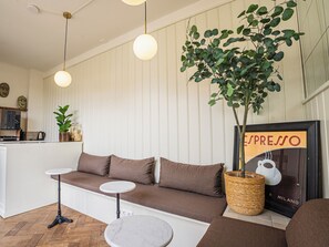 En modern inredning med en soffa, två sidobord, en hängande växt och en inramad skylt med texten ”espresso”.