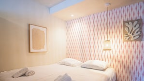 Une chambre d’hôtel avec un lit, des oreillers, un tableau encadré, un papier peint à motifs et un luminaire fixé au mur.