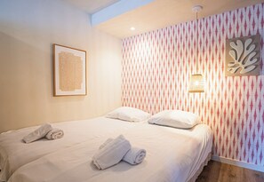 Hotellihuone, jossa on sänky, tyynyjä, kehystetty taideteos, kuviollinen tapetti ja seinään kiinnitetty valaisin.