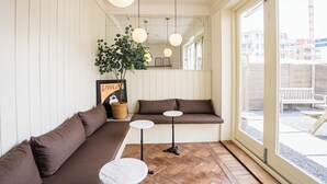 Un intérieur moderne avec un canapé, deux petites tables, des luminaires suspendus, une plante en pot et une grande fenêtre.