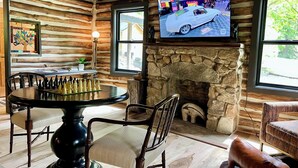 A log cabin interior with a stone fireplace, a chess table, and a television displaying a car. - Unique, renovated, historic log cabin in charming Hendersonville (Hendersonville)