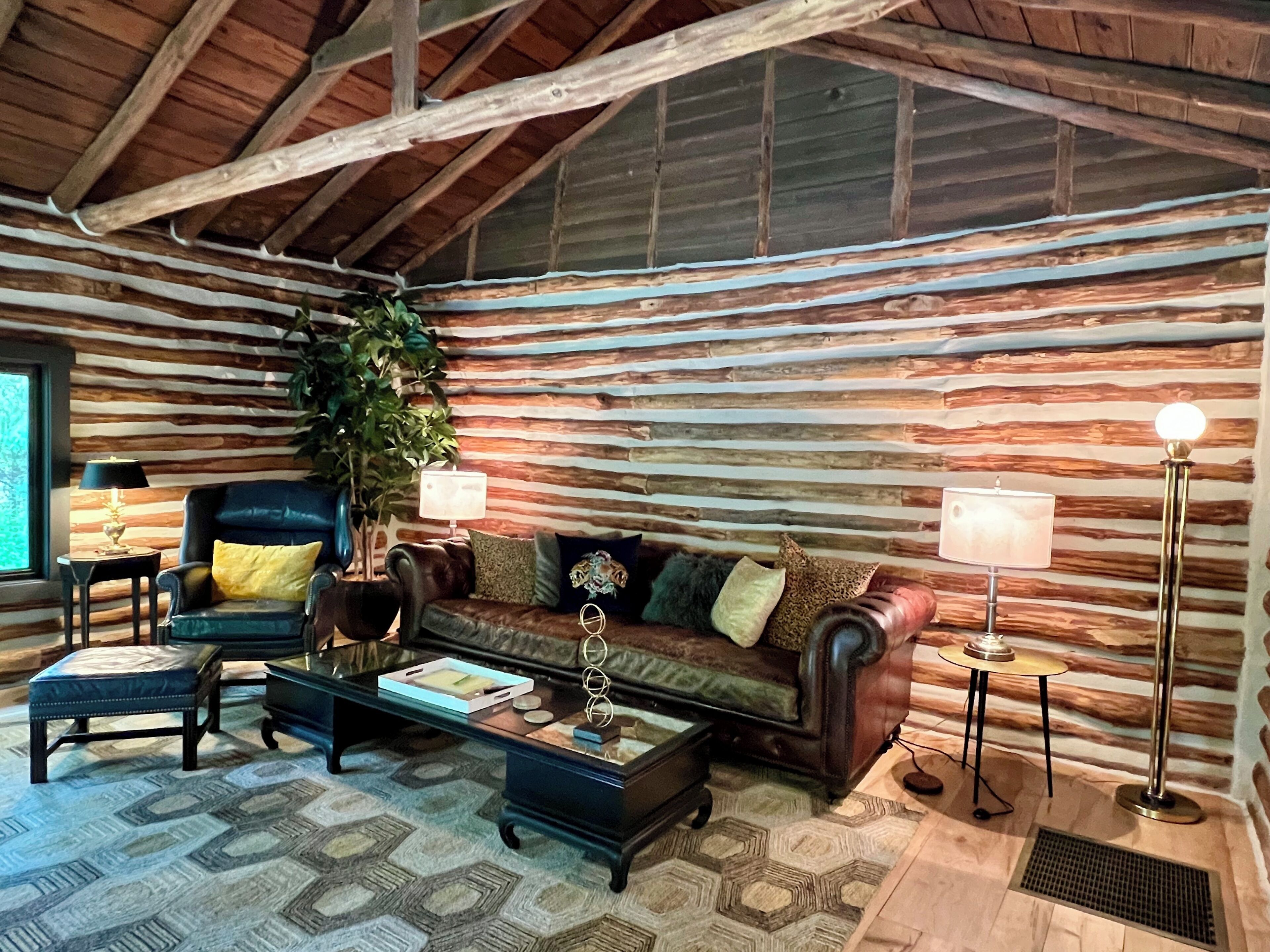 A log cabin interior with a leather sofa, two armchairs, a coffee table, and a lamp.