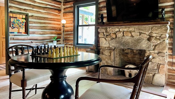 A log cabin interior with a dining table, chairs, a fireplace, a television, and a window with a view. - Unique, renovated, historic log cabin in charming Hendersonville (Hendersonville)