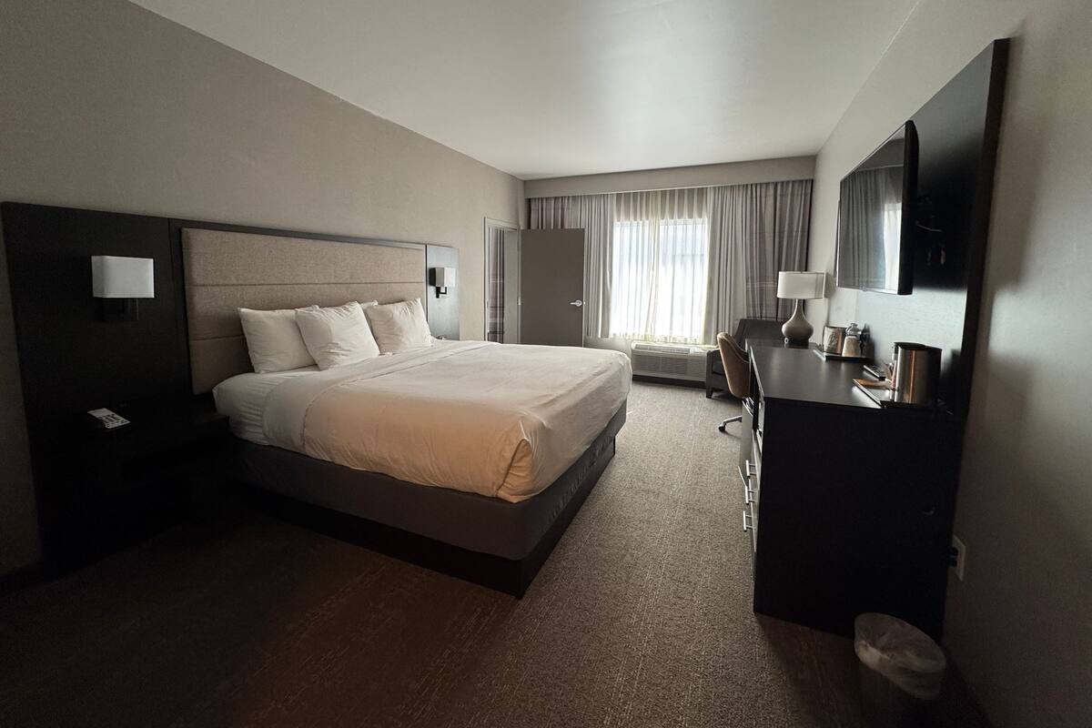 Ein Hotelzimmer mit einem großen Bett, einem Schreibtisch, einem Sessel, einem Kleiderschrank und einem Fernseher.