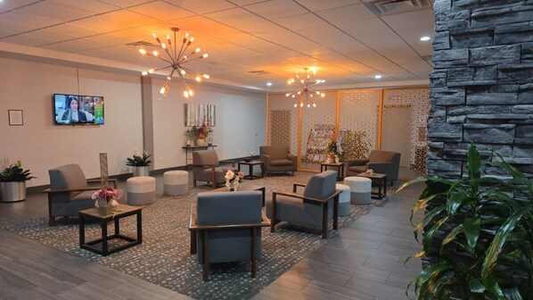 A lobby with seating, a TV, decorative plants, and a stone wall.