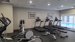 Un gimnasio con cintas de correr, bicicletas estáticas y una máquina de remo.