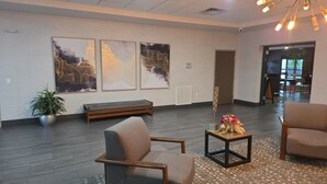 Un hall con un banco, dos sillones, una mesita con flores y tres obras de arte enmarcadas en la pared.