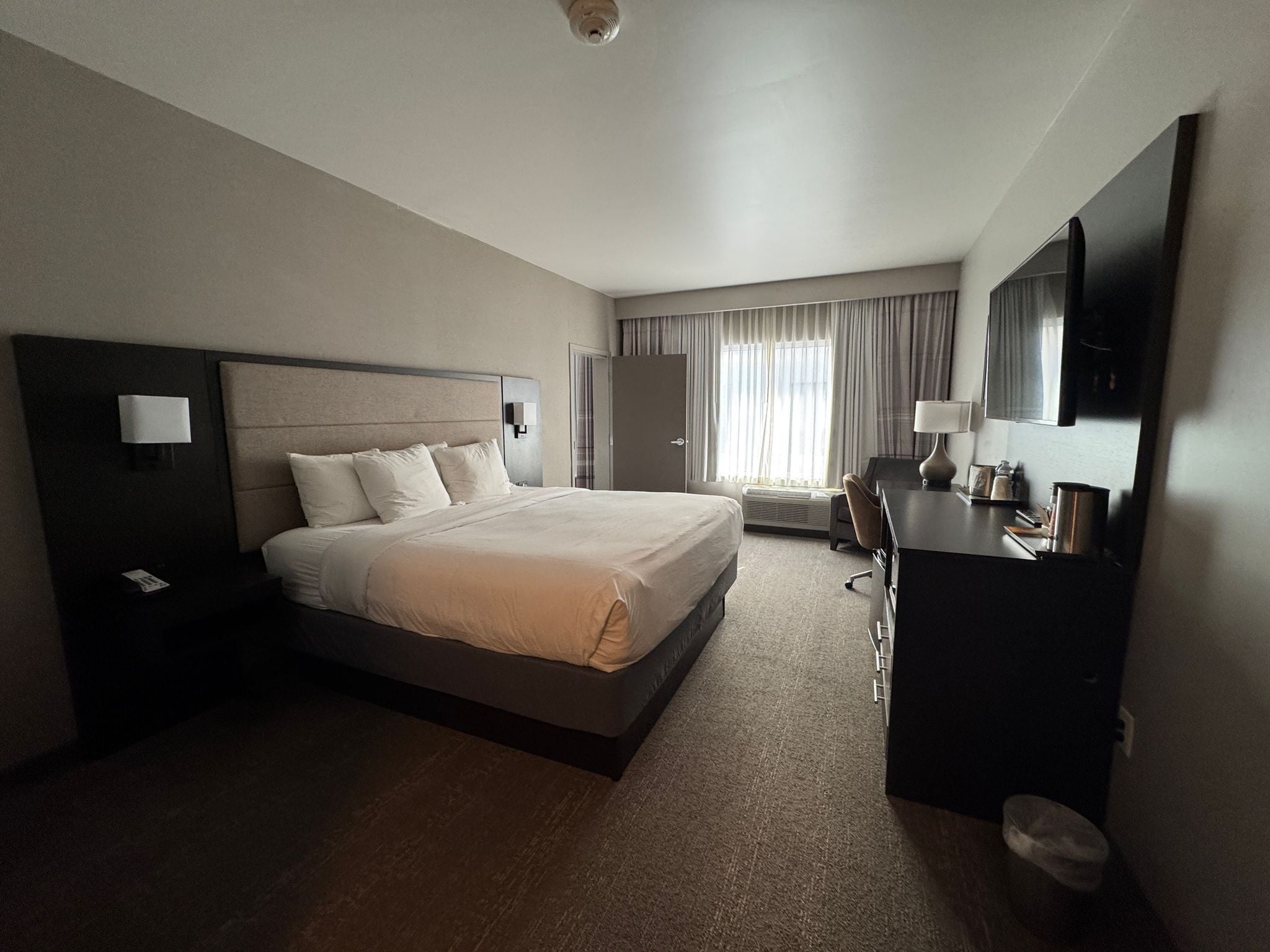 Una camera d'albergo con un letto grande, una scrivania con una sedia, una televisione a schermo piatto, un comodino e una finestra con tende.