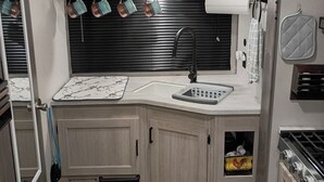 Une cuisine de taille réduite avec des meubles en bois, un plan de travail noir, un évier avec un robinet et une cuisinière.