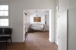 A room with a wooden floor, a bench, a bed, and a hanging light fixture. - Acassuso Suites (Acassuso)