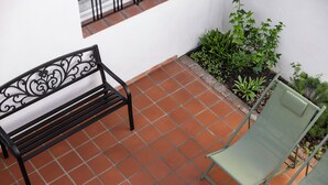 A terrace with a black metal bench and a green chair, surrounded by a white wall and a small garden with green plants. - Acassuso Suites (Acassuso)