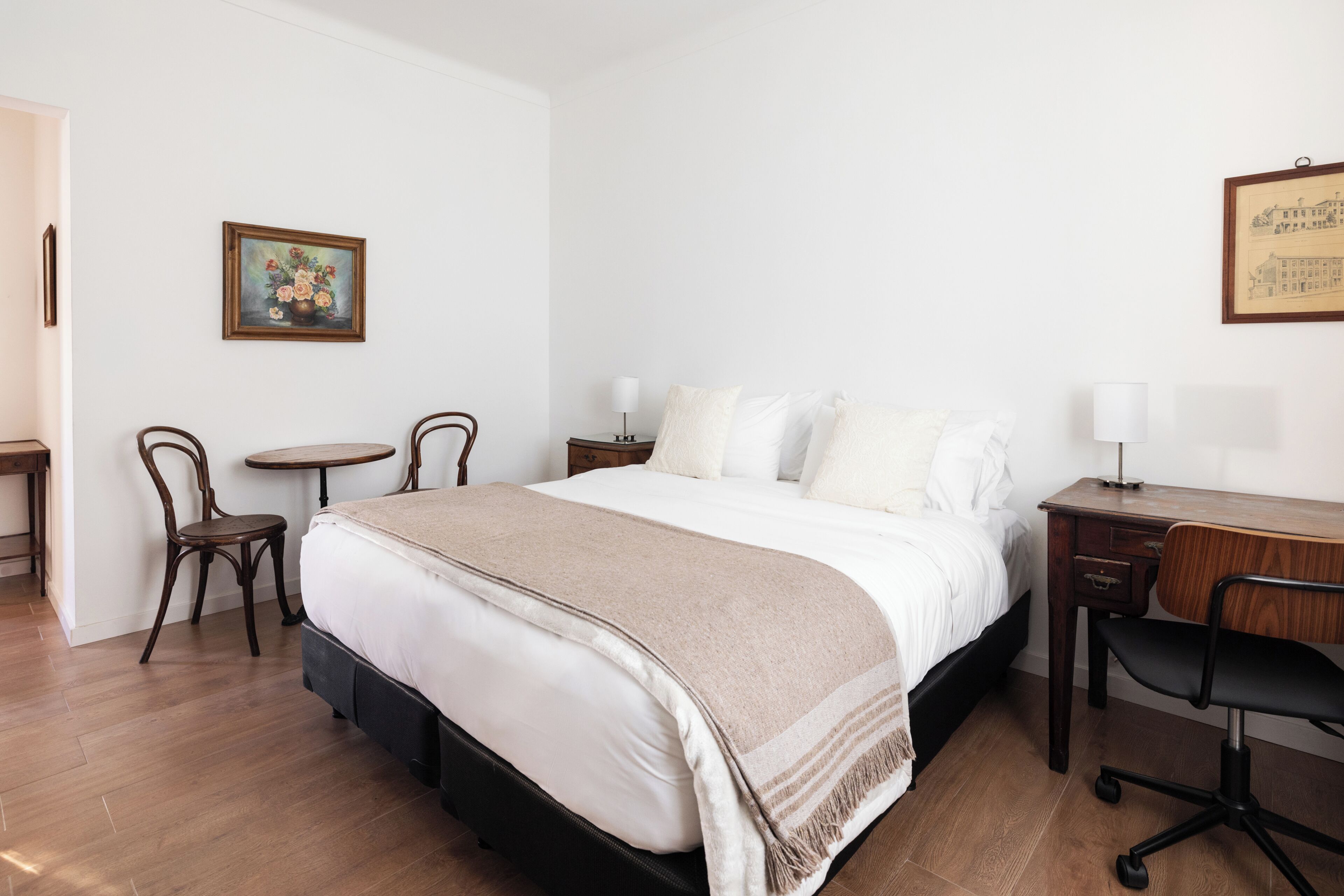 A bedroom with a bed, bedside tables, a desk, a chair, and a small table.