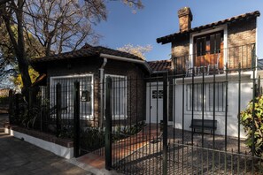 Una casa de dues plantes amb façana de maó, una tanca de metall negre i un petit porxo amb una banca.