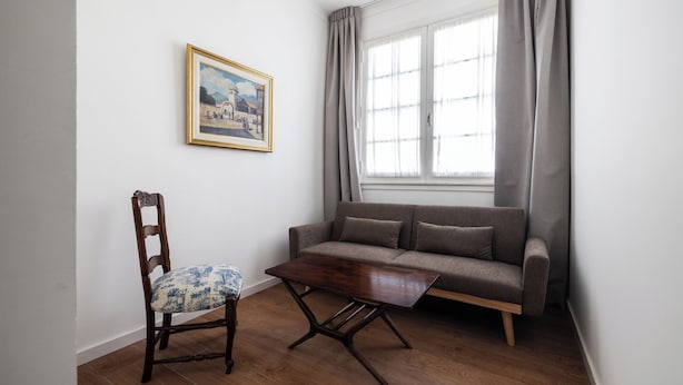 A room with a wooden floor, a sofa, a chair, a table, a window with curtains, and a framed picture on the wall. - Acassuso Suites (Acassuso)