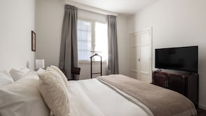 A hotel room with a bed, a television, a chair, and a window with curtains. - Acassuso Suites (Acassuso)