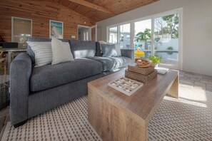 A modern living room with a grey sofa, wooden coffee table, and large windows. - 4BR Family Oasis - Heated Pool - Walk to Beach (St. Pete Beach)