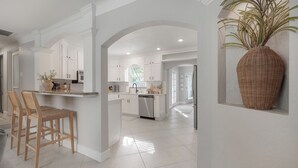 Una cucina moderna con mobili bianchi, un'isola centrale e un grande vaso in vimini.