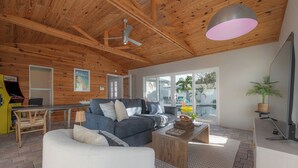 Un soggiorno moderno con soffitto in legno, un divano grigio, una poltrona bianca, un tavolino in legno e una grande finestra con vista sull'esterno.