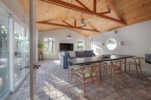 A spacious living area with a wooden ceiling, a TV, a sofa, and a dining table with chairs. - 4BR Family Oasis - Heated Pool - Walk to Beach (St. Pete Beach)