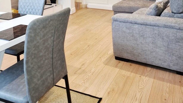 Una sala de estar moderna con sofá, una mesa de comedor con sillas, un cuadro en la pared y luces empotradas en el techo.
