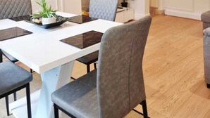 Un comedor moderno con una mesa blanca, sillas tapizadas de gris y un cuadro en la pared.
