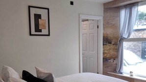 Un dormitorio con cama, almohadas, una puerta, una ventana y un cuadro en la pared.