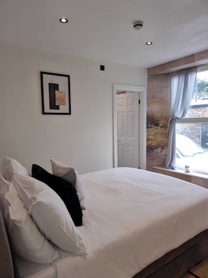 Une chambre à coucher avec un lit, des oreillers, une porte, une fenêtre et un tableau au mur.