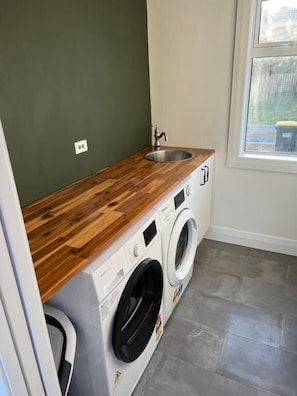 A compact laundry room with a wooden countertop, a sink, and two front-loading washing machines.